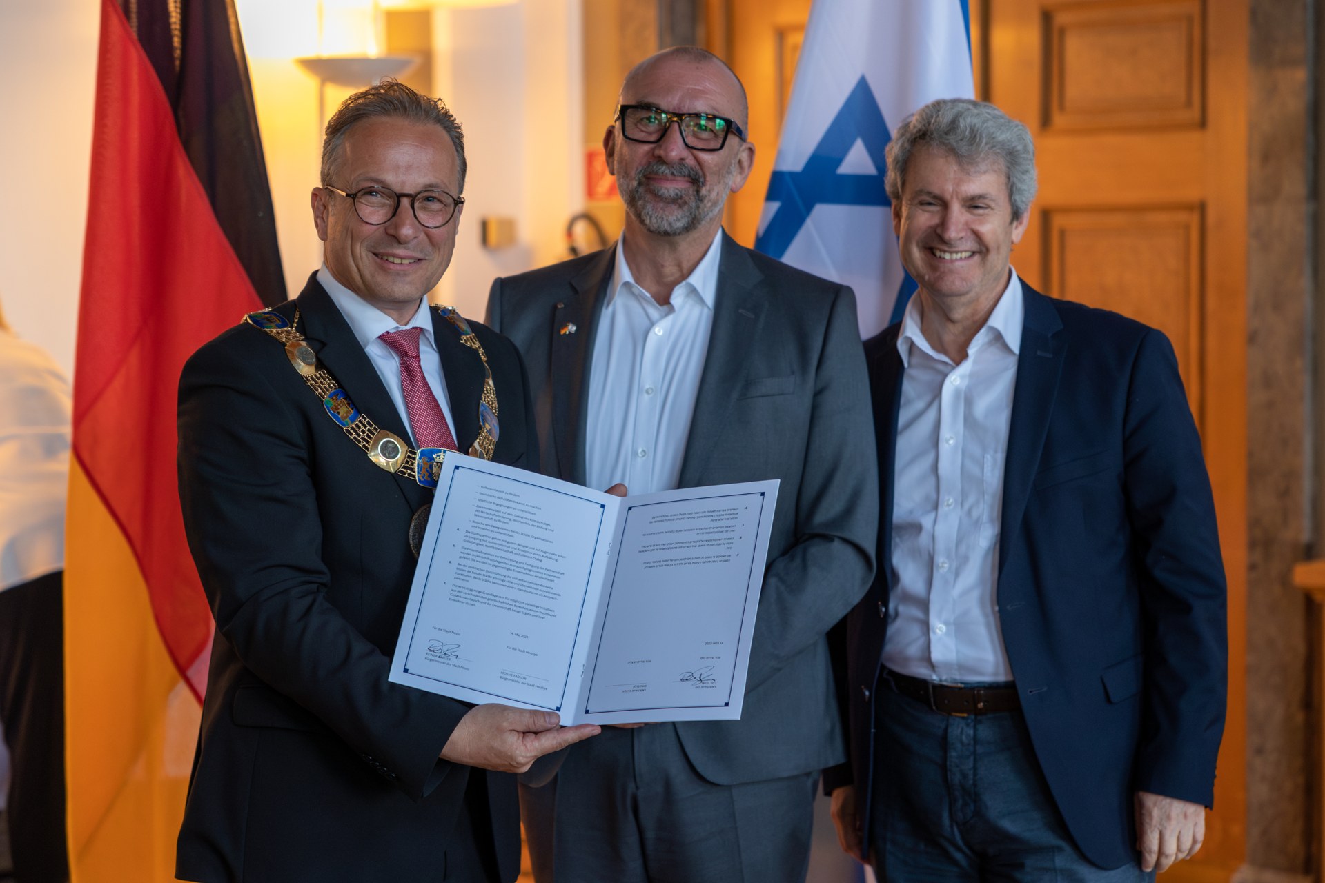 Herzliya Unterzeichnung Urkunde Städtepartnerschaft (1).jpg Bürgermeister Reiner Breuer, Bert Römgens und Dr. Oded Horowitz stehen von den Flaggen Deutschlands und Israels. Bürgermeister Breuer hält den unterschriebenen Partnerschaftsvertrag hoch.